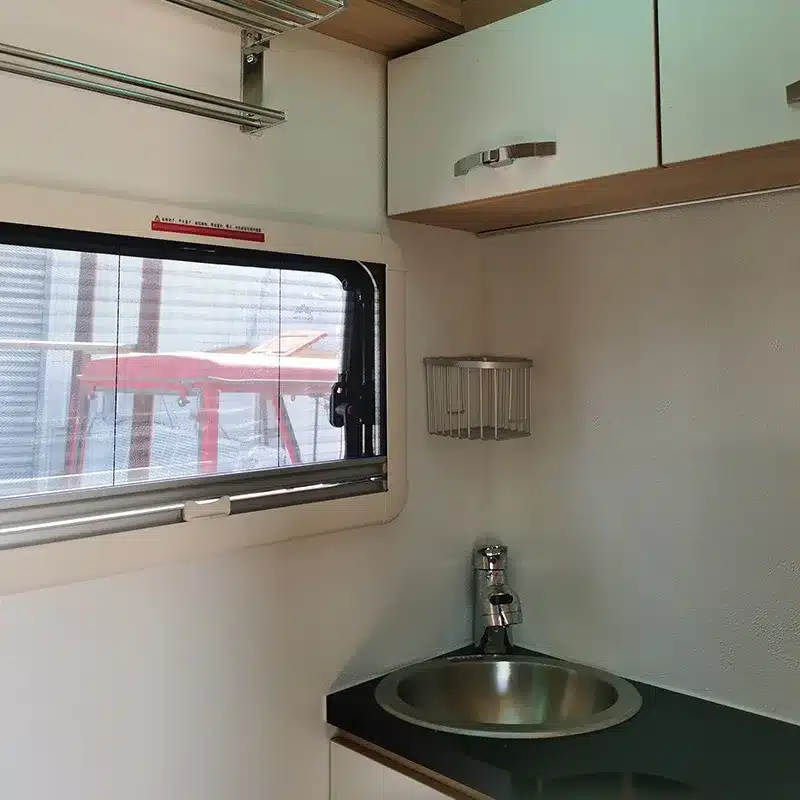Innenraum des Black Rhino T12 mit Edelstahlspüle, Ablage und Oberschränken an einem Fenster.