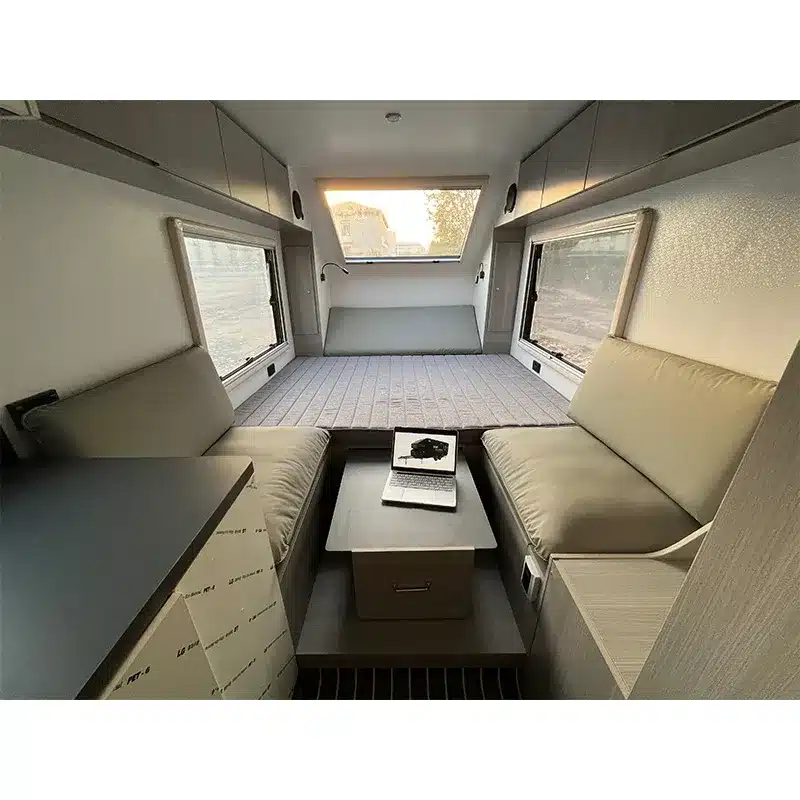 Innenansicht des Black Rhino T19 Offroad-Caravans mit Sofaecke, verstellbarem Tisch und großem Bett im Hintergrund