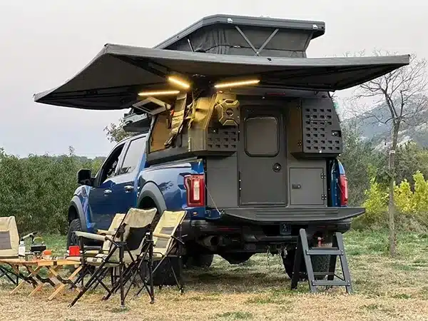Pickup mit Black Stone Ilmenite Camper, Aufstelldach geöffnet und Außenküche im Einsatz auf Campingplatz.