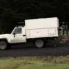 Bliss Mobil 8 Foot Expeditionskabine montiert auf einem weißen Pick-up im Gelände vor Waldkulisse.