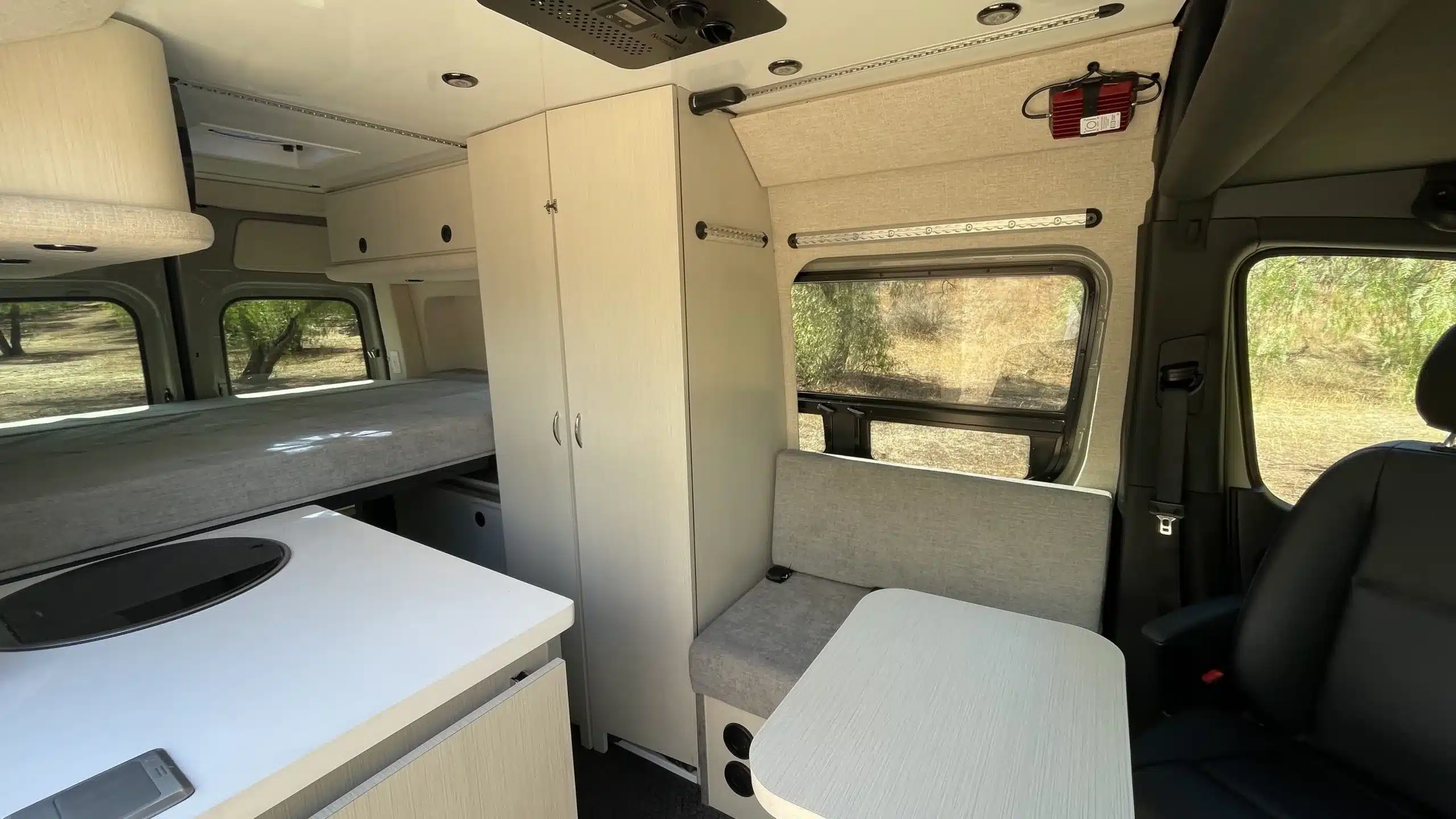 Innenraum eines Burn Adventure-Vans mit Sitzbank, Tisch, Küchenzeile und festem Plattformbett im Heck