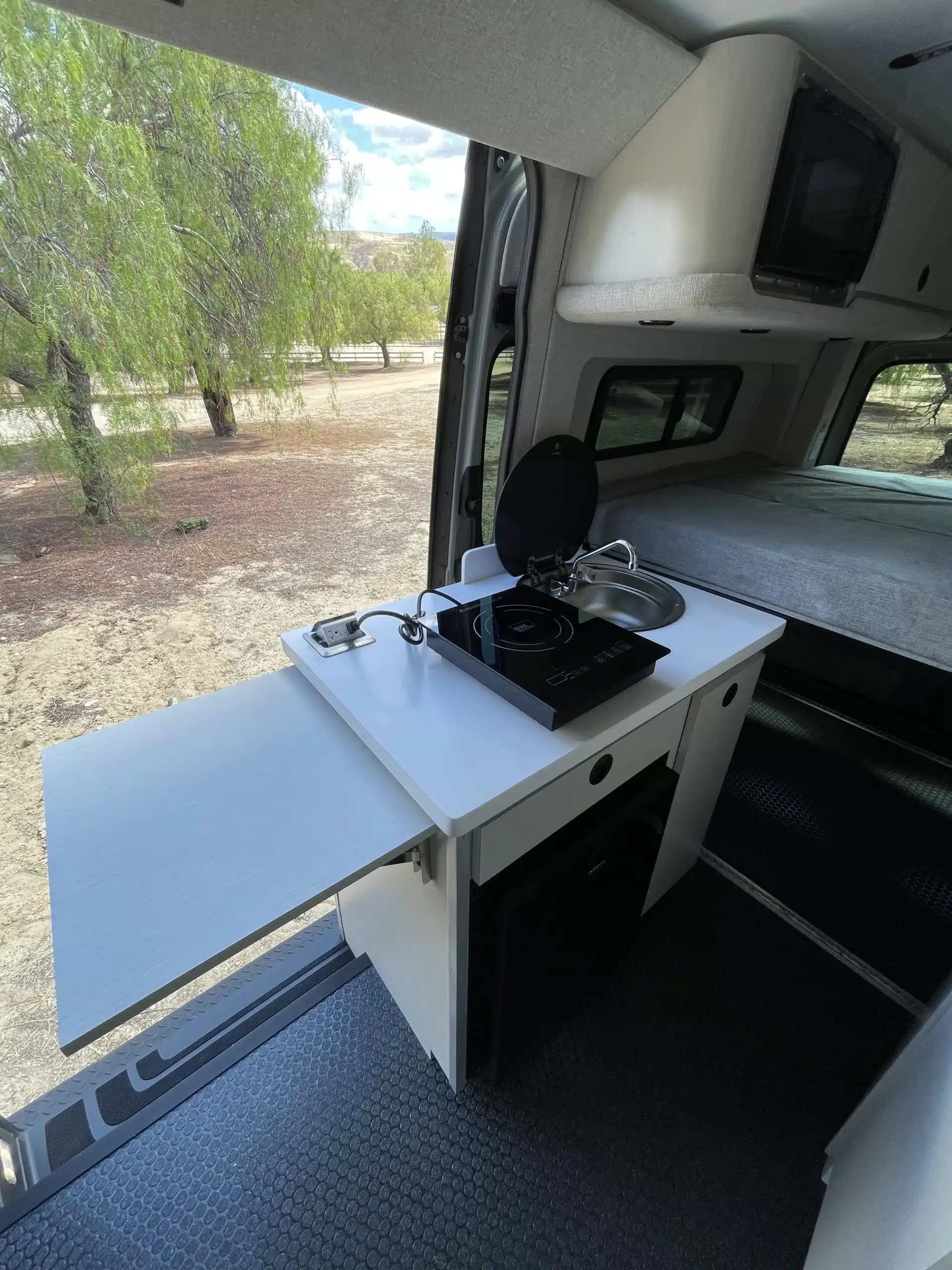 Küchenzeile mit Induktionskochfeld, Spülbecken und ausziehbarer Arbeitsplatte im Burn Adventure-Van auf Sprinter 4x4 Basis.
