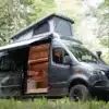 Kastenwagen Camper mit geöffnetem Aufstelldach und ausgebautem Innenraum, geparkt im Wald.