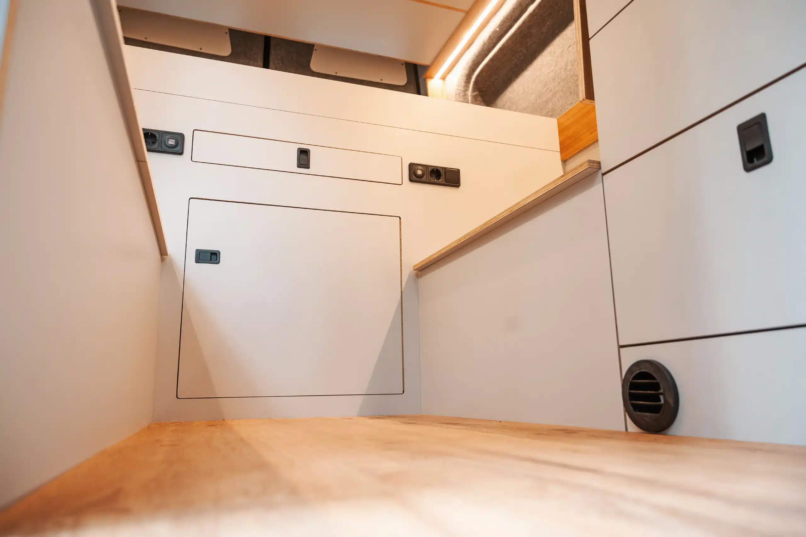 Innenraum eines Camperausbau X mit hellen, integrierten Möbeln, Stauraum und Steckdosen.