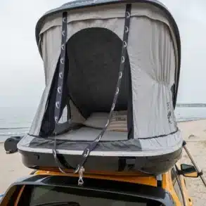 Hartschalen-Dachzelt Urban Badger montiert auf dem Dach eines gelben Fahrzeugs am Strand, geöffnet und bereit zum Camping.