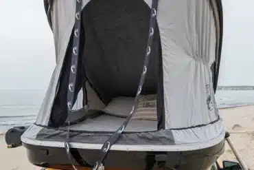 Hartschalen-Dachzelt Urban Badger montiert auf dem Dach eines gelben Fahrzeugs am Strand, geöffnet und bereit zum Camping.