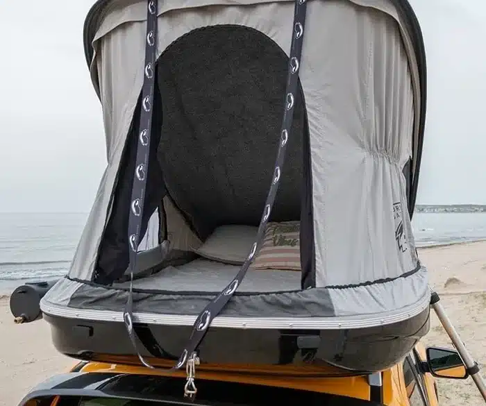 Hartschalen-Dachzelt Urban Badger montiert auf dem Dach eines gelben Fahrzeugs am Strand, geöffnet und bereit zum Camping.