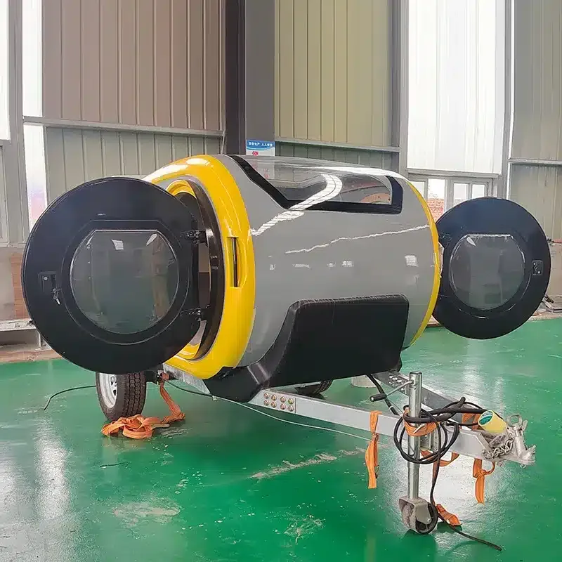 Kompakter, zylinderförmiger Wohnanhänger mit gelben Akzenten und seitlichen Rundtüren in einer Halle