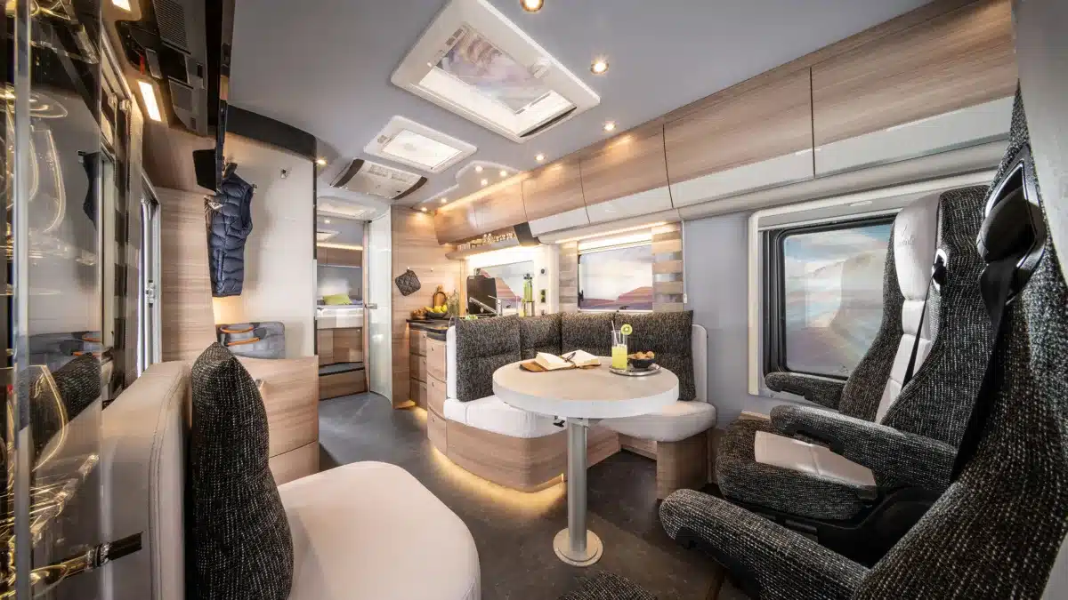 Luxuriöser Wohnbereich im Reisemobil Concorde Credo Graphite Edition mit modernen Sitzmöbeln, Tisch und Design-Küche.