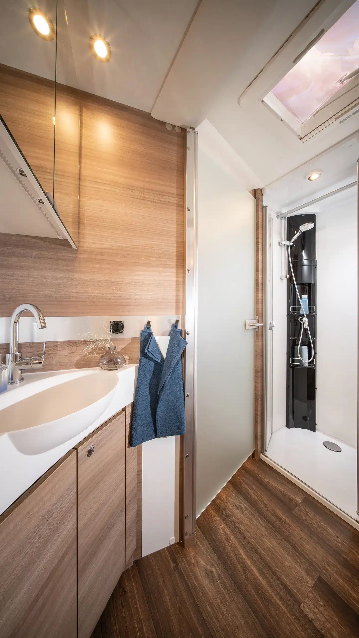 Badezimmer mit Holzdekor, Waschbecken, Spiegel, Handtüchern und moderner Dusche im Concorde Cruiser Daily Reisemobil