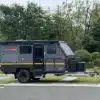 Seitenansicht des Conquer Off-Road Trailer 590, angehängt an ein SUV, auf einem Parkplatz mit Bäumen im Hintergrund.