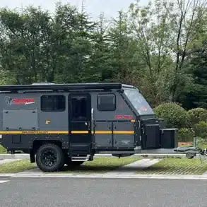 Seitenansicht des Conquer Off-Road Trailer 590, angehängt an ein SUV, auf einem Parkplatz mit Bäumen im Hintergrund.