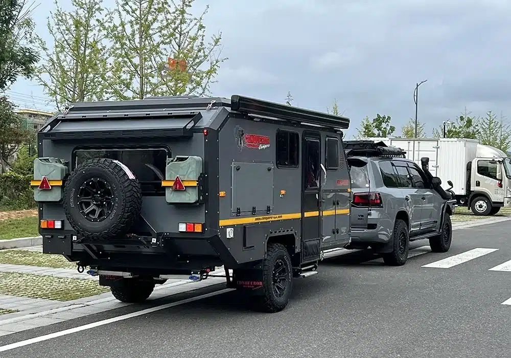 Conquer Off-Road Trailer 590 angehängt an ein geländegängiges Zugfahrzeug auf einer Straße im Grünen