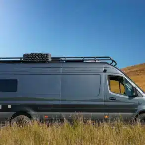 Seitenansicht des Crozier Beyond2 Campervans auf Mercedes-Benz-Sprinter-Basis, parkend in einer grasbewachsenen Landschaft, mit Dachträger und Notrad.