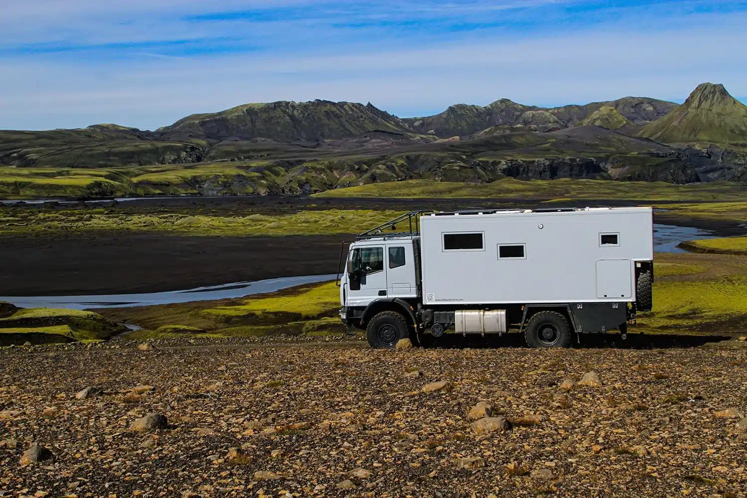 Expeditions-LKW mit Wohnaufbau steht in einer weiten, naturbelassenen Landschaft vor Bergen.