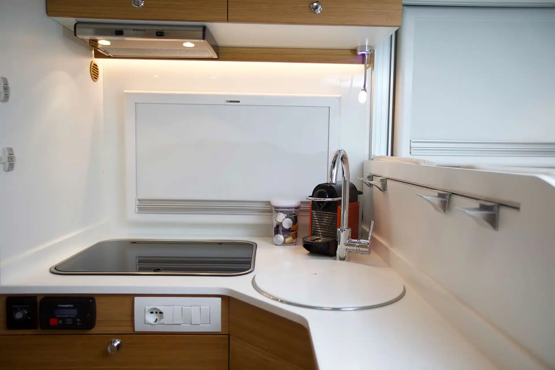 Innenansicht einer hochwertigen Küchenzeile in einem Expeditions-LKW mit edlen Holzoberflächen, moderner Spüle und Kaffeemaschine.
