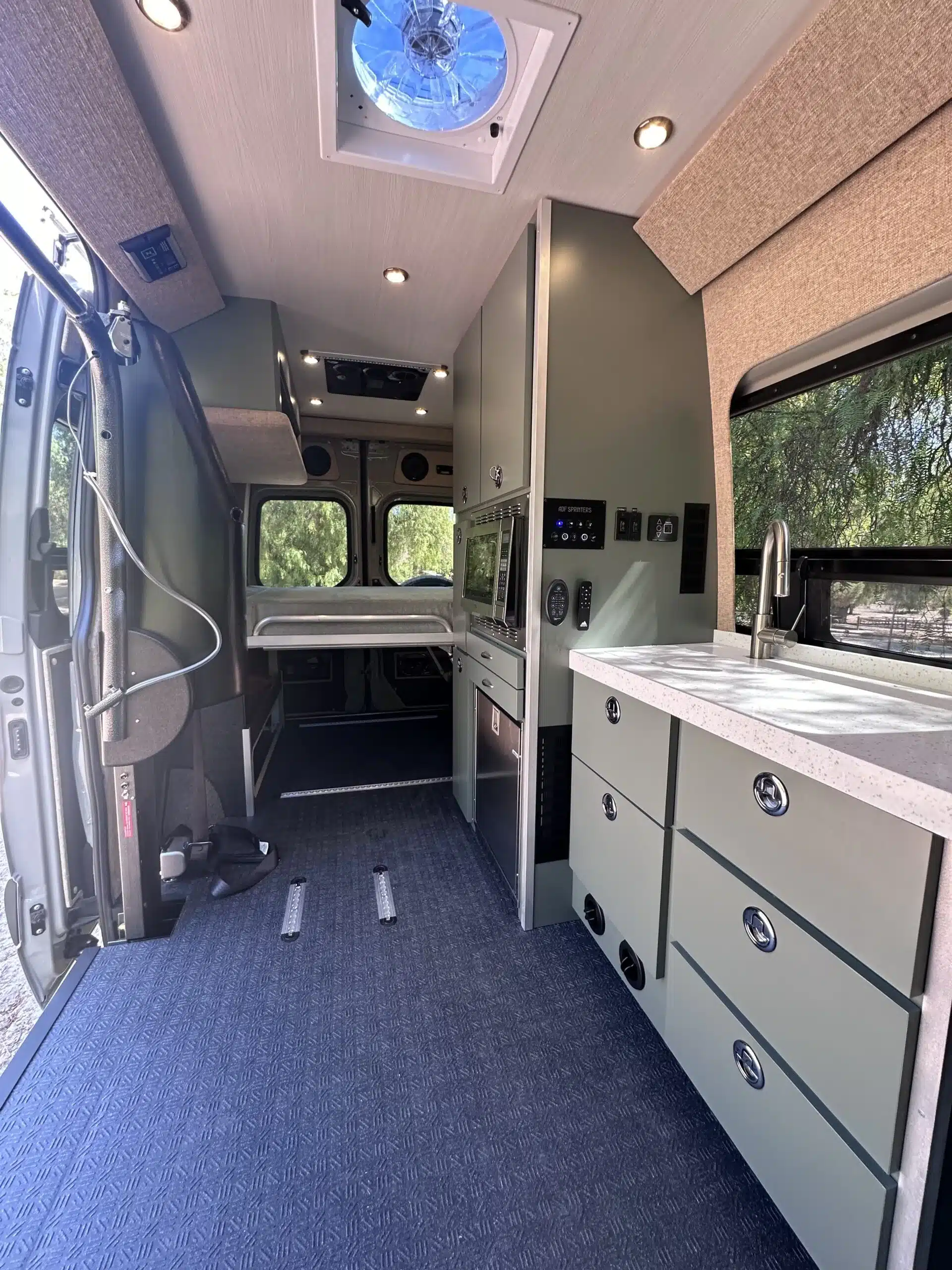 Blick in den barrierefreien Innenraum eines Mercedes Sprinter Campervans mit tiefergelegtem Küchenblock, elektrisch verstellbarem Bett und großzügigem Durchgang für Rollstuhlnutzung.