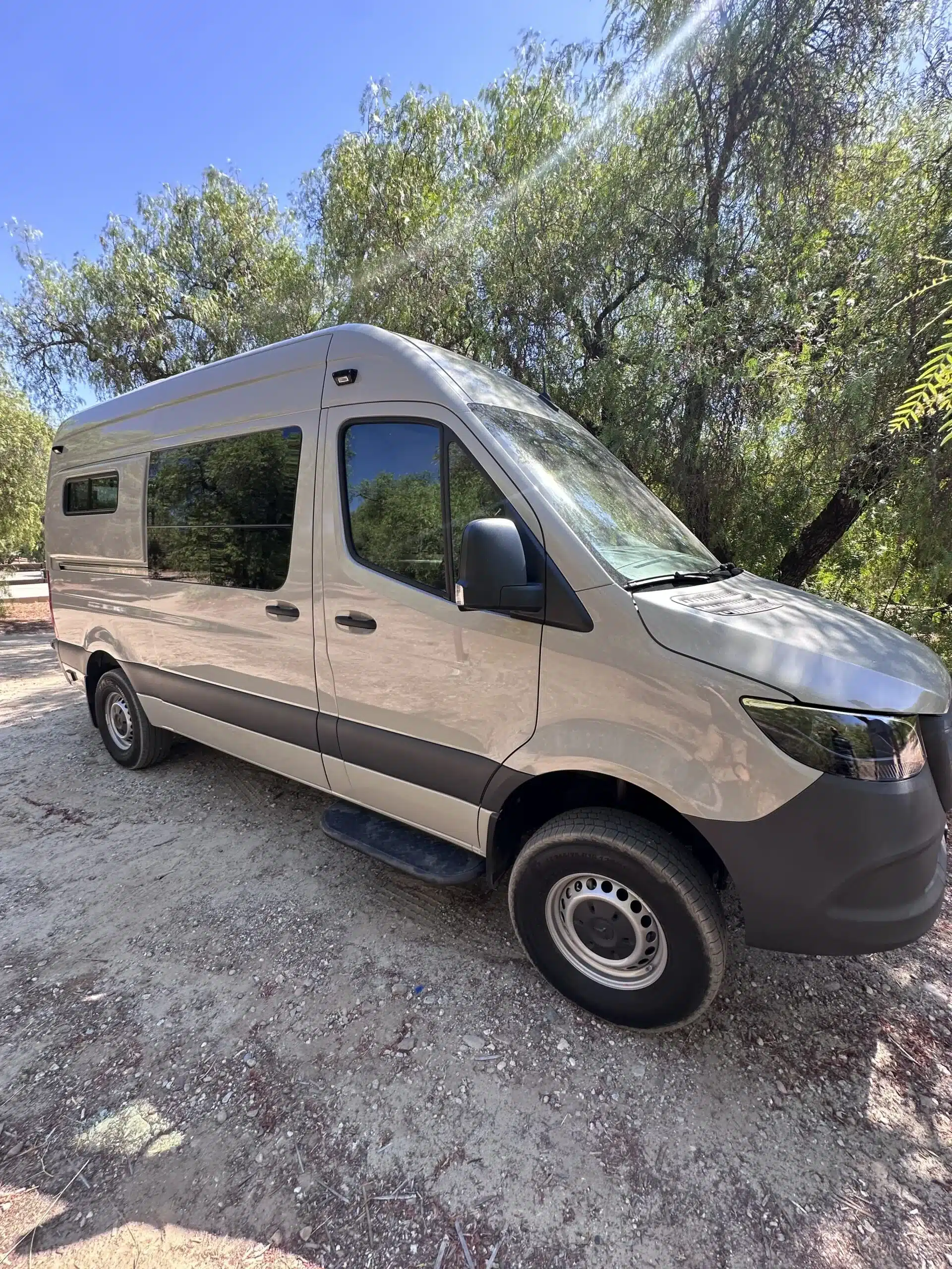 Seitenansicht eines barrierefreien Campervans auf Basis eines Mercedes Sprinter 144, geparkt unter Bäumen im Freien.