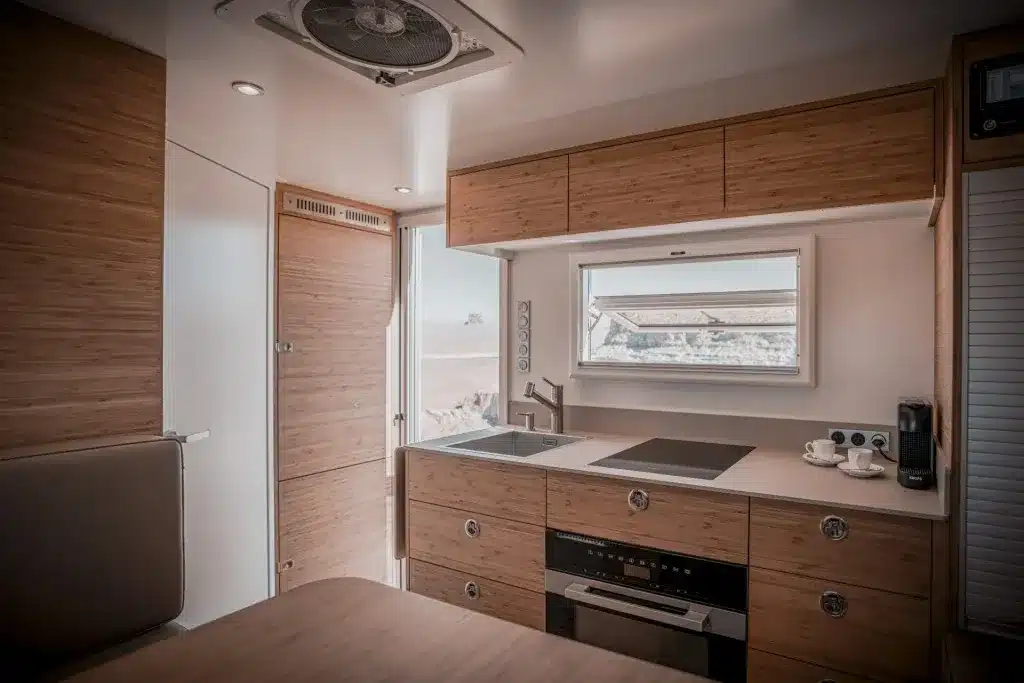 Moderne Küchenzeile mit Induktionskochfeld, Spülbecken, Ofen und Stauraum im Expeditionswohnmobil 4 900 MM CREW 2