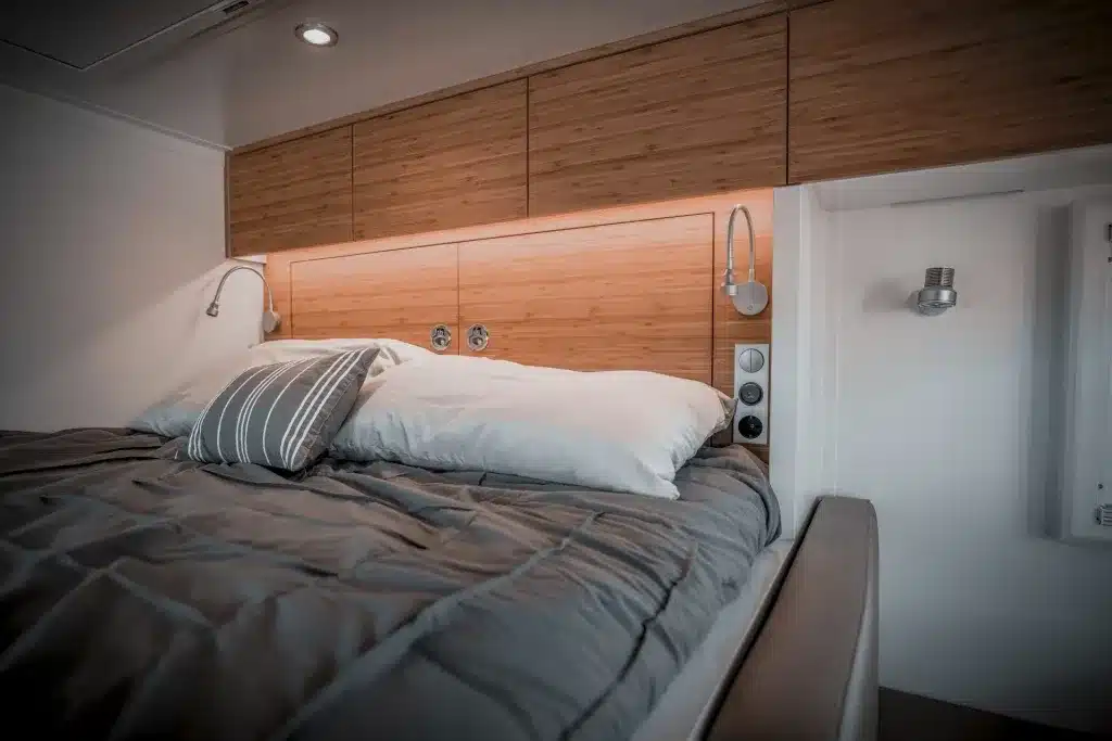 Modernes Doppelbett mit Holzverkleidung und Ober- sowie Leselampen im Expeditionsmobil