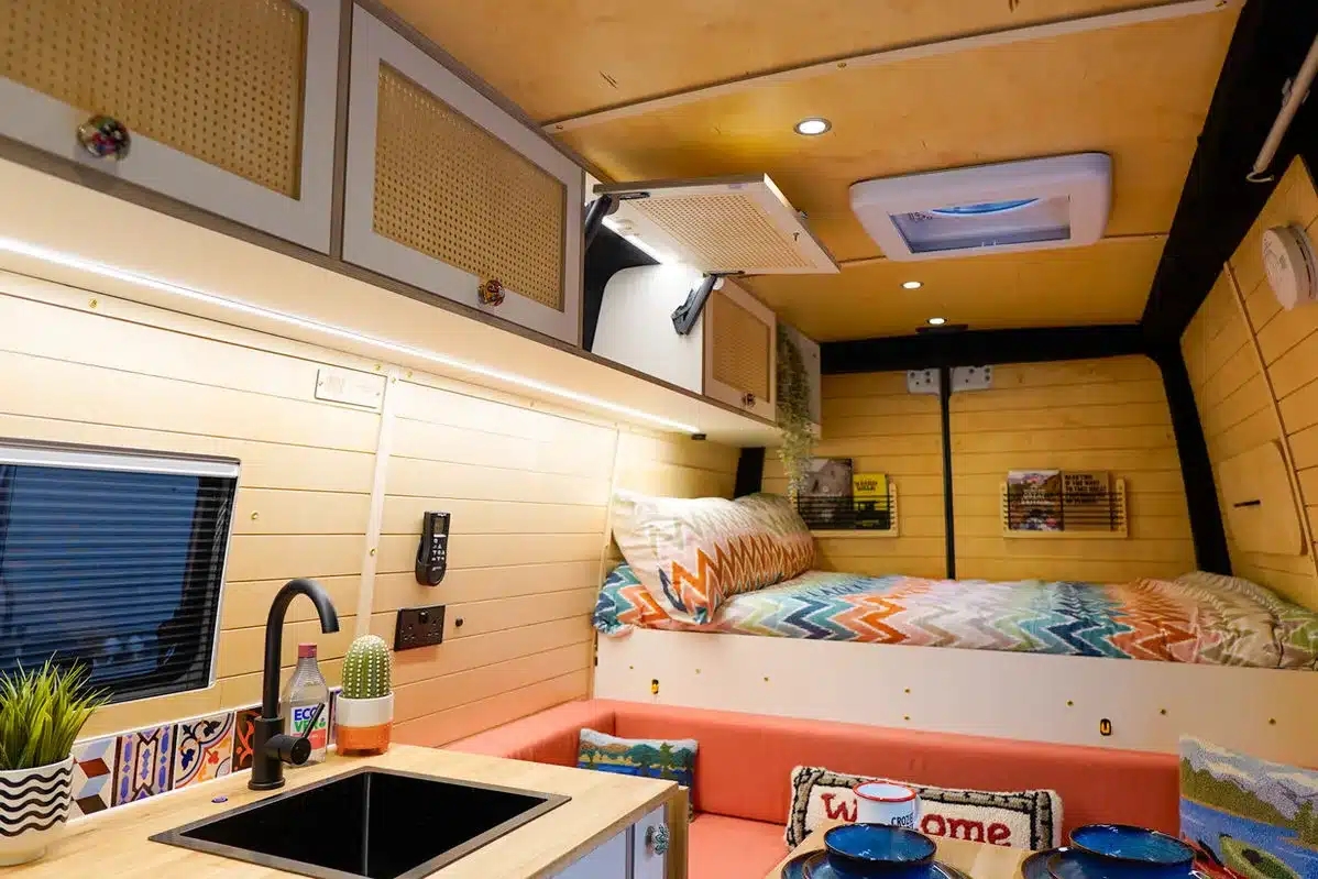 Moderner, individuell gestalteter Innenraum eines Campervans mit Bett, Sitzbank und Küchenzeile