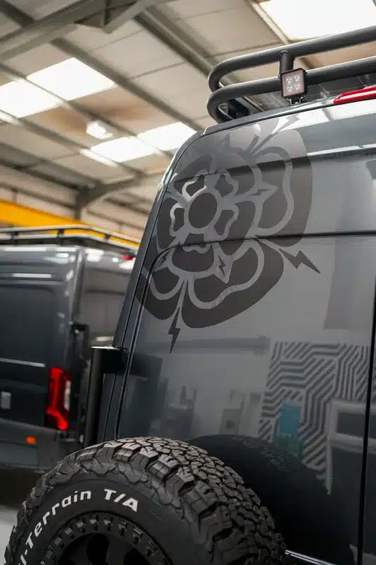 Heckansicht eines maßgeschneiderten Mercedes-Benz Sprinter mit grafischem Motiv und Offroad-Reifen in einer Werkshalle