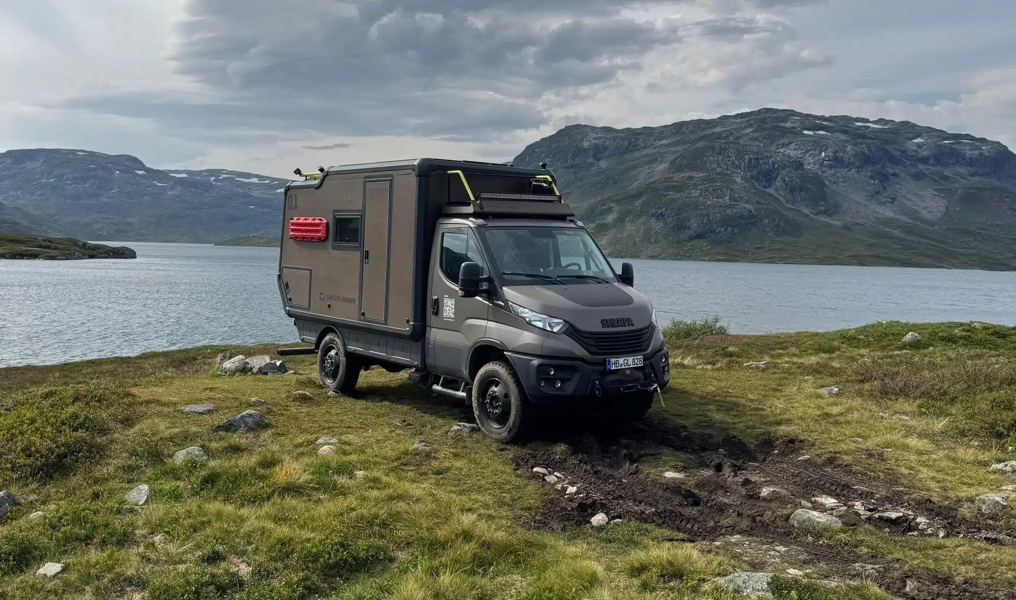 Greenlander Sherpa Expeditionsfahrzeug auf naturnahem Offroad-Gelände mit See und Bergen im Hintergrund
