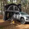 Hotomobil Atlas Cabin Box auf einem VW Pickup, ausgeklappt als Campinglösung mit Zelt und Feuerstelle im Wald.