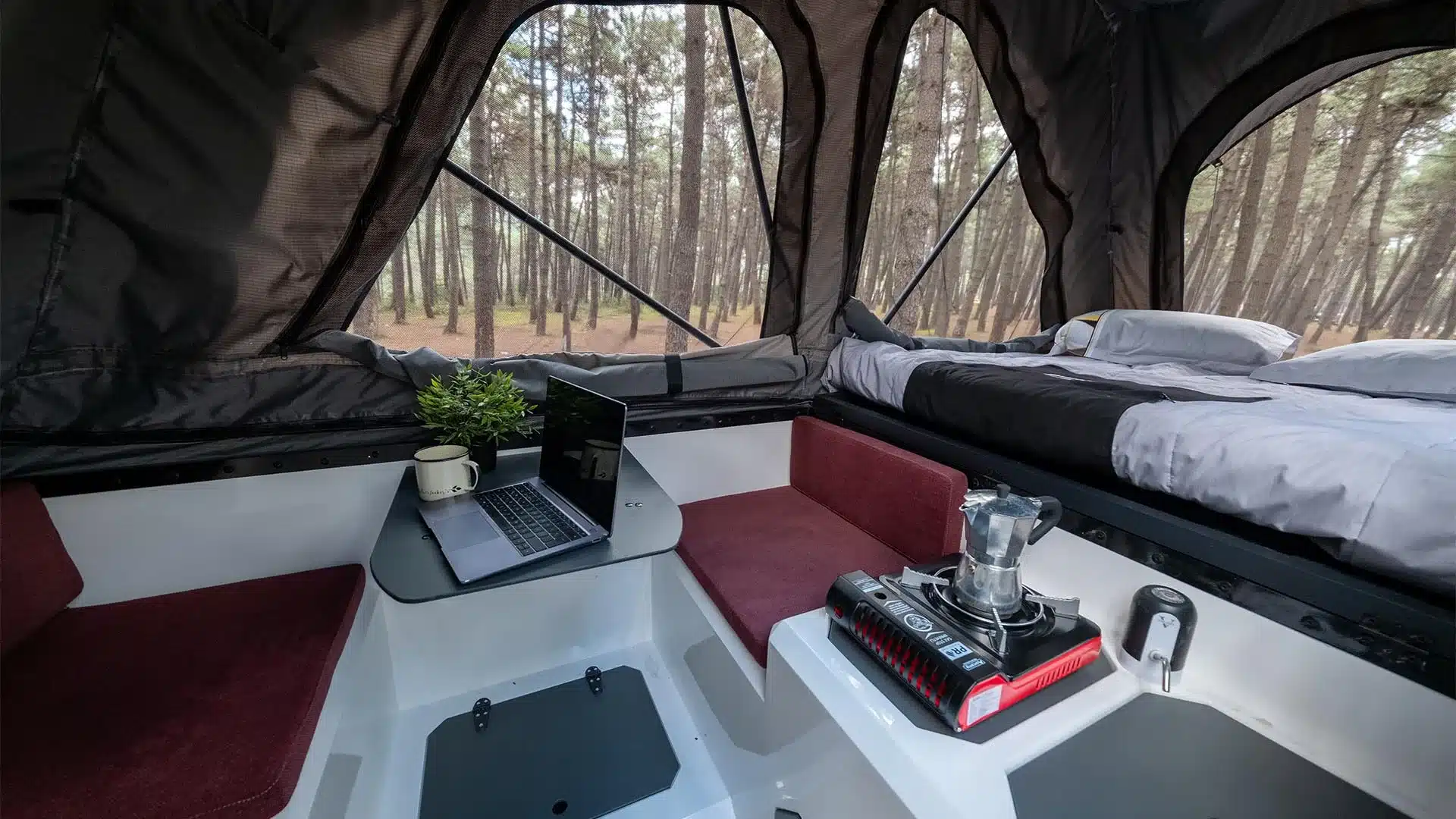 Innenraum der Hotomobil Atlas Cabin Box mit Sitzbereich, ausgeklapptem Schlafplatz und Küchenmodul.