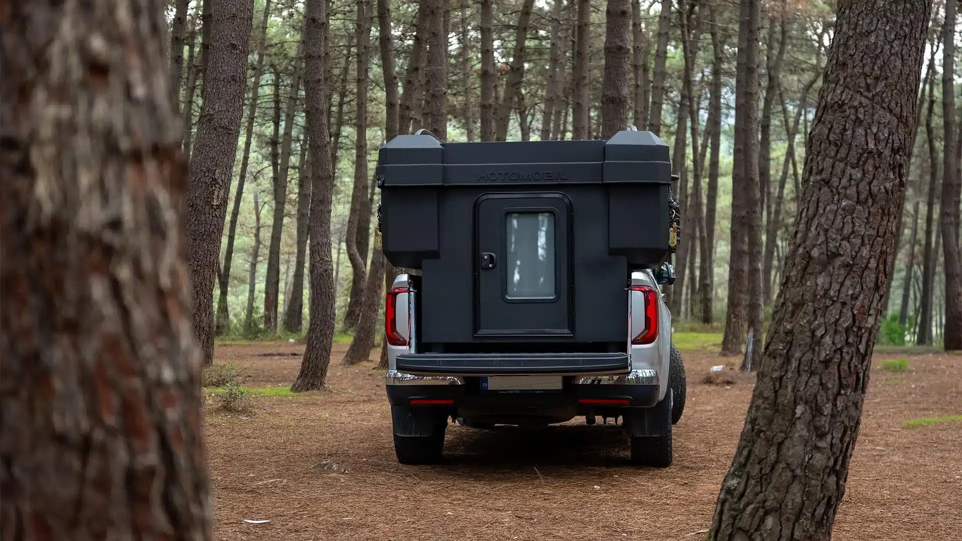 Heckansicht einer Hotomobil Atlas Cabin Box auf einem Pickup, stehend im Wald.