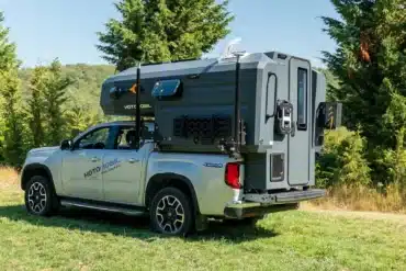 Ein silberfarbener Pickup mit montierter, monolithischer GFK-Wohnkabine von Hotomobil steht auf einer Wiese im Grünen