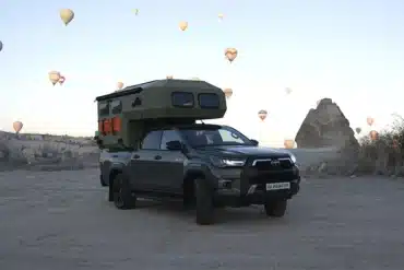 Pickup mit Hotomobil Gladiator Wohnkabine steht im Freien, im Hintergrund steigen zahlreiche Heißluftballons auf