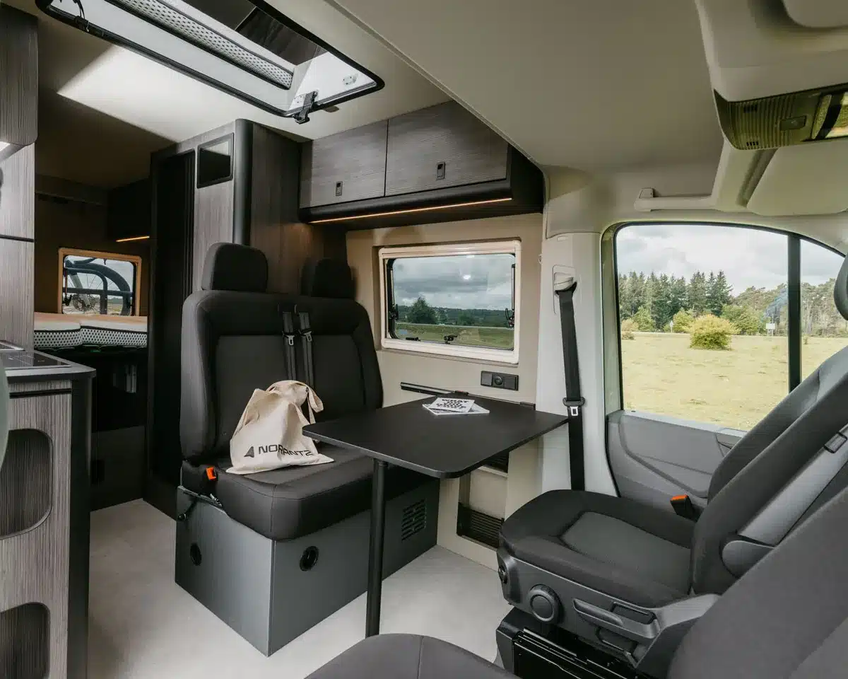 Moderner Wohnbereich im IPAR Furgoneta Camper NORANTZ mit Sitzbank, Fahrer- und Beifahrersitz sowie Blick nach draußen
