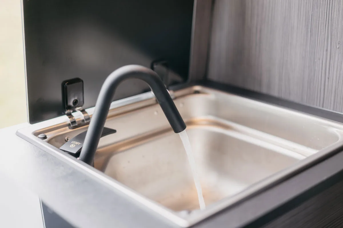 Nahaufnahme einer Edelstahlspüle mit geöffnetem Wasserhahn in einem Camper.