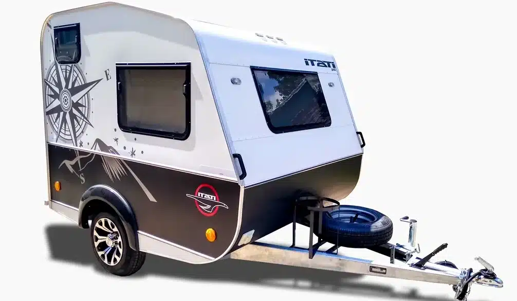 Der ITATI 240 TFi Wohnwagen steht auf einem hellen Hintergrund, zeigt moderne Dekorelemente und ein Reserverad an der Deichsel.