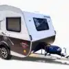 Der ITATI 240 TFi Wohnwagen steht auf einem hellen Hintergrund, zeigt moderne Dekorelemente und ein Reserverad an der Deichsel.