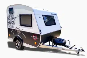 Der ITATI 240 TFi Wohnwagen steht auf einem hellen Hintergrund, zeigt moderne Dekorelemente und ein Reserverad an der Deichsel.