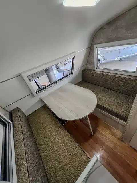 Sitzgruppe mit zwei Polsterbänken und Tisch im ITATI 240 TFi Wohnwagen, Fenster im Hintergrund.