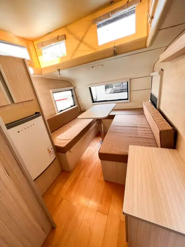 Innenraum des Itati 380 TLi Wohnwagens mit Sitzgruppe, Tisch, Kühlschrank und geöffnetem Hubdach.