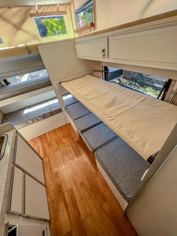Innenraum des Itati 460 TLi Caravans mit ausklappbaren Betten, Sitzpolstern, Stauraum und großen Fenstern