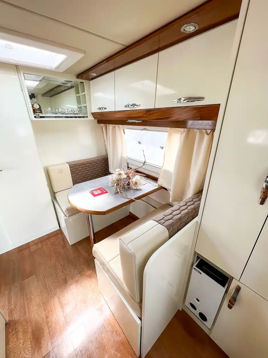 Essbereich und Innenraum des Itati Avant-Garde Deluxe Caravans mit Sitzgruppe, Fenster und Oberschränken.