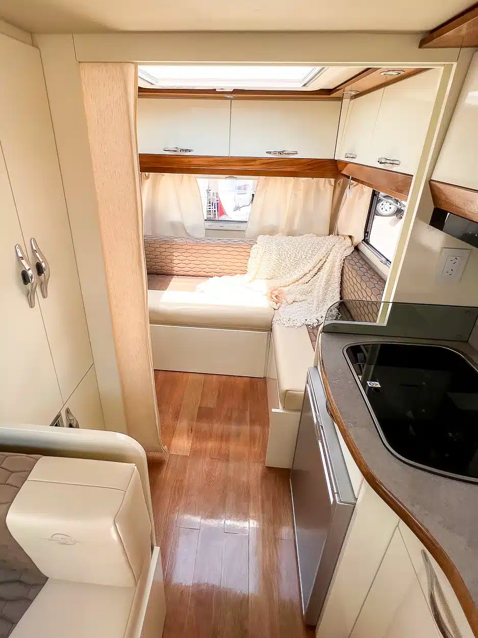 Der moderne, helle Innenraum eines luxuriösen Itati Avant-Garde Deluxe Caravans mit Sitzgruppe, Küche und Holzoptik-Boden.