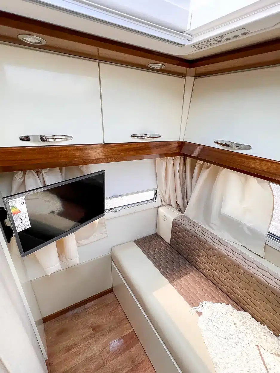 Wohnbereich mit Sitzbank, TV und Stauraummöbeln im Itati Avant-Garde Deluxe Caravan, Blick auf Dachfenster und Holzdetails.