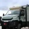 Iveco Daily 4x4 Expeditionsmobil in grün-grau mit individuellem Aufbau, davor steht eine Person.