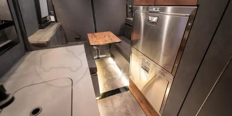 Blick in den Innenraum eines Iveco Daily 4x4 Campers mit Edelstahl-Küchenblock, Kompressor-Kühlschrank und Sitzgruppe.