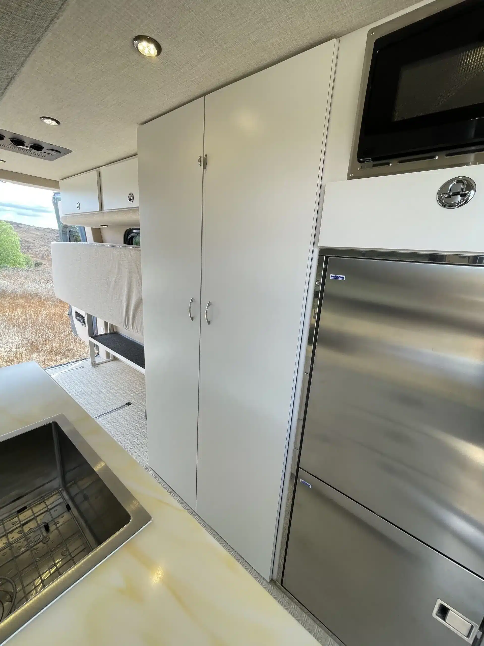 Moderne Küchenzeile mit Spüle, Kühlschrank und Mikrowelle im Jackson 4x4 Sprinter Van Innenraum