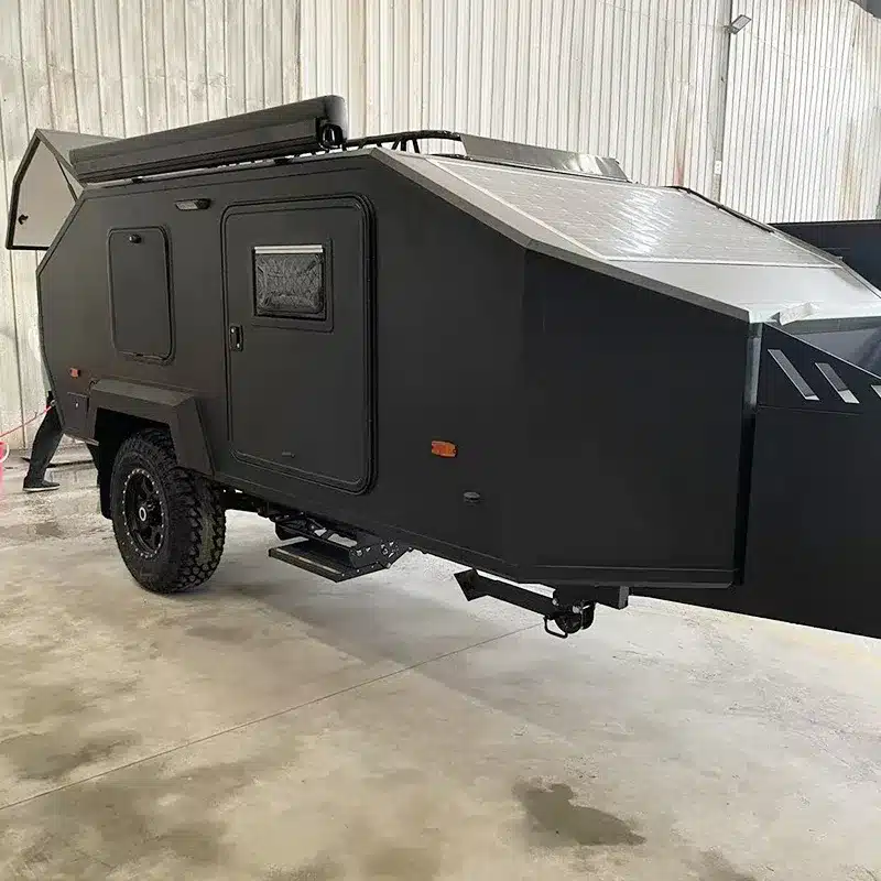 Schwarzer JR Black Rhino 2A Offroad-Reisewohnwagen mit Geländebereifung, abgestellt in einer Halle.