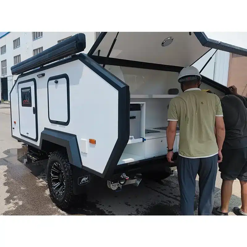 JR Black Rhino 2A Offroad-Campinganhänger mit geöffneter Heckküche und zwei Personen beim Einblick ins Küchenmodul.