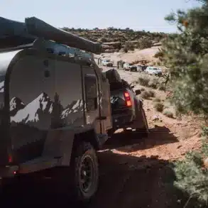 Offroad-Campertrailer, gezogen von einem Pickup, fährt auf einer matschigen, unbefestigten Strecke mit weiteren Fahrzeugen im Hintergrund