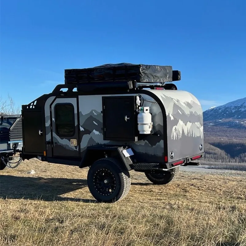 Seitenansicht eines JR Black Rhino VIC Offroad-Campertrailers mit Geländebereifung und Outdoor-Ausstattung in bergiger Landschaft.